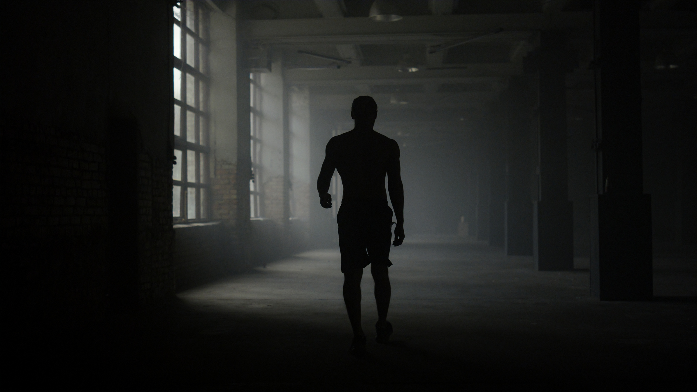 Man silhouette walking in dark corridor. Athlete taking break after workout